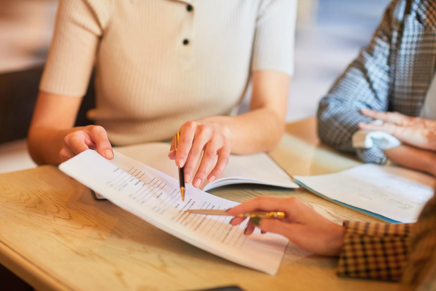 Two people reviewing a document together at a table, pointing at line items with pens, representing the importance of reading prepaid funeral contract details before signing
