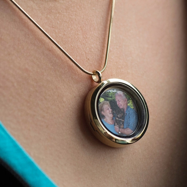 Bronze Round Photo Glass Pendant Necklace, available at Magnolia Cremations, shown worn, featuring a gold-tone stainless steel pendant with a hinged glass front displaying a treasured photo. Designed to securely hold ashes, engraving is available for added personalization.