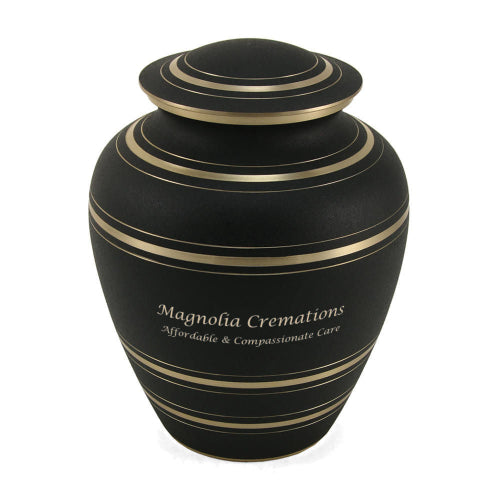 A full-size memorial urn with a matte black finish and gold accent stripes. The urn has a rounded shape with a domed lid, both featuring thin gold bands. Engraving is shown on the front, with personalization available.