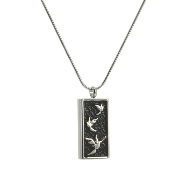 The Embossed Pewter/Onyx Doves Memorial Necklace, available at Magnolia Cremations, is a stainless steel pendant featuring silver doves in flight against a textured black background. Designed to discreetly hold a small portion of ashes, this elegant piece symbolizes peace and remembrance. The pendant comes with a matching 19-inch chain, and engraving is available for personalization.