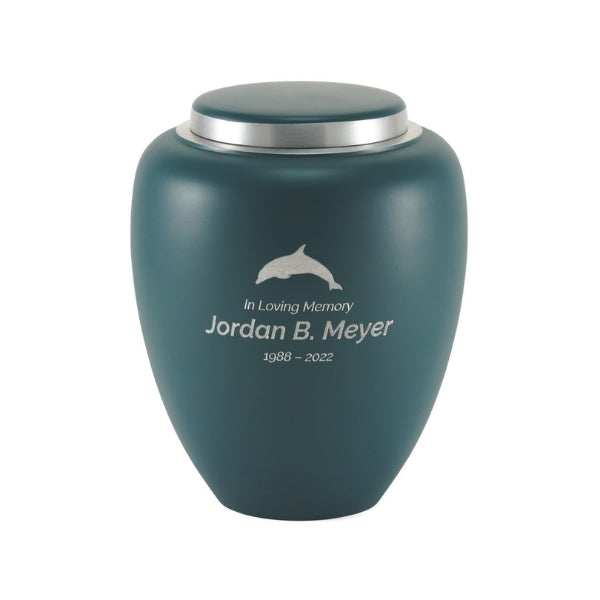 A matte teal-sapphire blue memorial urn with a silver lid, featuring an engraved design. The engraving includes text and a dolphin symbol. Engraving is shown and available.