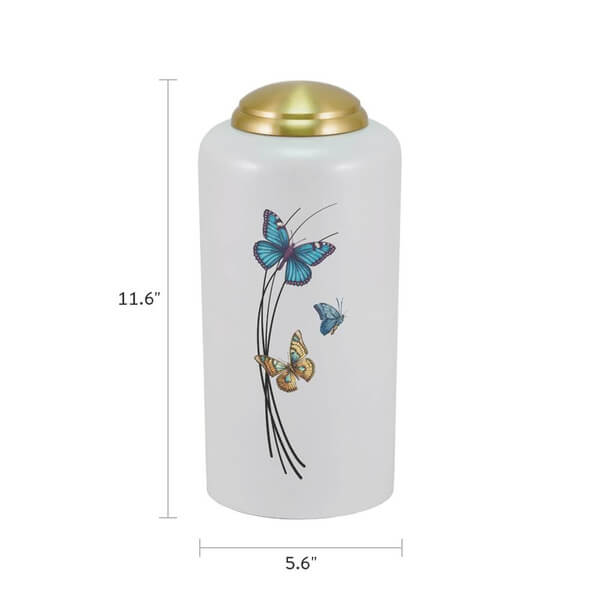 White cremation urn with a gold domed lid, measuring 11.6 inches tall and 5.6 inches wide. The front features a design of three colorful butterflies—blue, teal, and orange—fluttering around thin black curved lines.