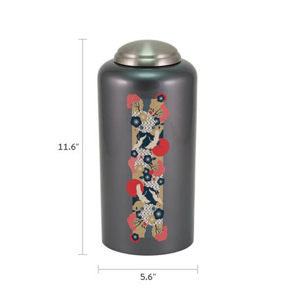 Dark gray cremation urn with a metallic lid, featuring a vertical decorative strip with a Japanese-style design of cranes, red sun motifs, and floral patterns in red, navy blue, white, and beige. Dimensions are labeled: 11.6 inches tall and 5.6 inches wide.