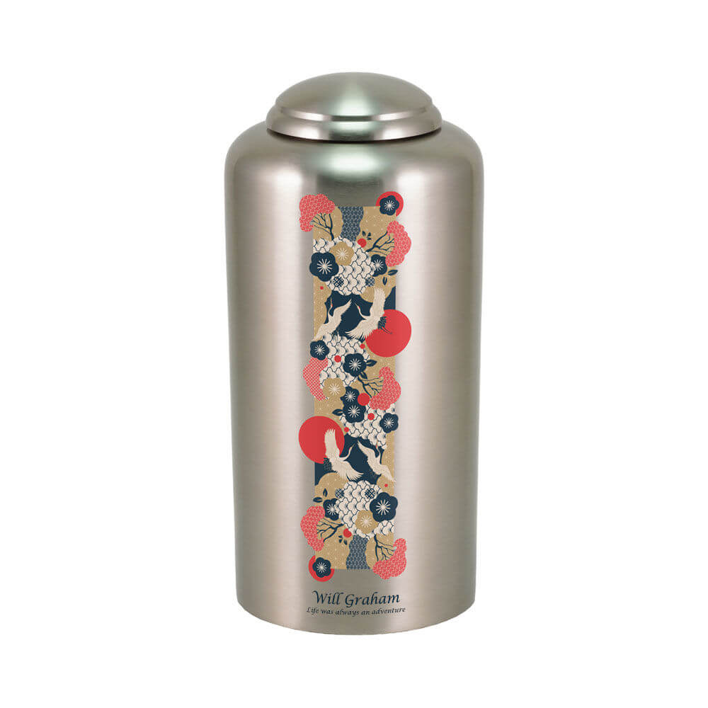 Silver cremation urn featuring a vertical Japanese-inspired design with flying white cranes, red sun motifs, and floral patterns in red, navy blue, cream, and gold. Near the base, there is engraving shown.