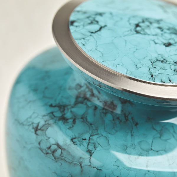 A close-up of a teal blue marble-patterned urn, highlighting its glossy finish, intricate black veining, and silver-tone rim. The detailed shot captures the smooth curvature of the urn’s lid and upper portion, emphasizing its elegant craftsmanship.