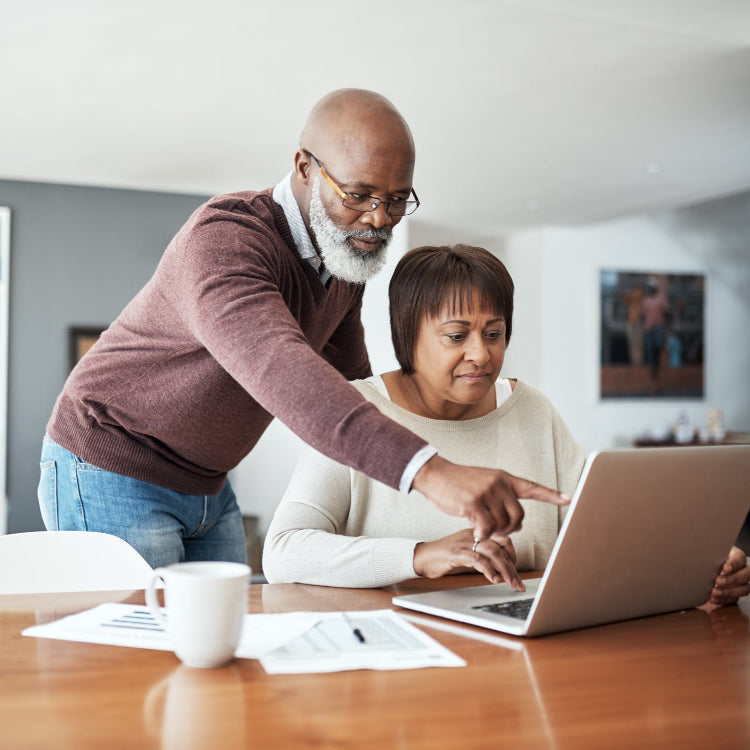 African American couple working on a computer at the dining room table with a living room in the background.