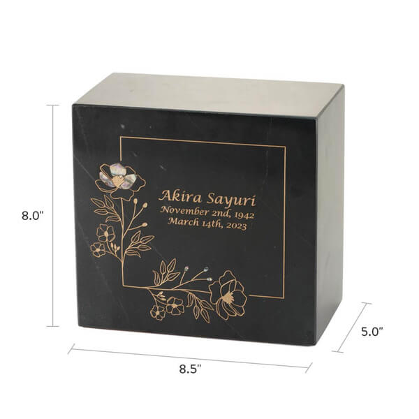 Black marble cremation urn with gold floral line art and one iridescent flower inlay; optional engraving is shown with name and dates; dimensions are 8.0 inches high, 8.5 inches wide, and 5.0 inches deep.