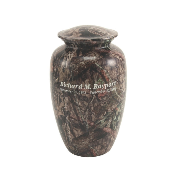 Mossy Oak Camo Memorial Urn by Magnolia Cremations, featuring an authentic woodland camouflage design with branches, leaves, and pine accents. This full-size aluminum urn is a perfect tribute for a nature enthusiast or outdoorsman. Engraving is shown as an available option.