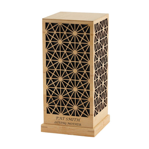 The Palazzo memorial urn, available at Magnolia Cremations, is shown in a close-up image. This extra-large urn is made from bamboo and black MDF, featuring an intricate geometric lattice design on all visible sides. A custom engraving is displayed on the base, highlighting the option for personalization. The urn's natural wood tones and detailed craftsmanship create a sophisticated and timeless tribute.