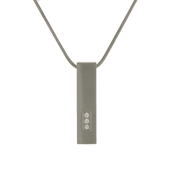 The Pewter Pillar with Cubic Zirconia Memorial Necklace, available at Magnolia Cremations, is a sleek stainless steel pendant with a brushed silver finish and three shimmering cubic zirconia accents. Designed with a hidden compartment, this modern pillar-shaped pendant holds a nominal amount of ashes, providing a meaningful way to cherish a loved one's memory. The necklace includes an engraving option, showcased in other images, for personalization and comes with a matching 19-inch chain.