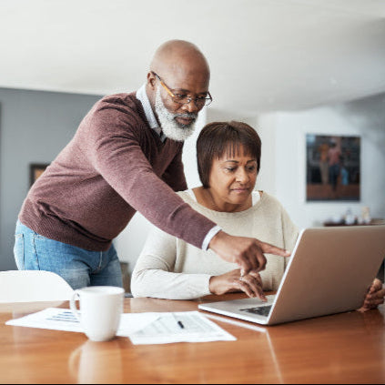African American couple working on a computer at the dining room table with a living room in the background.