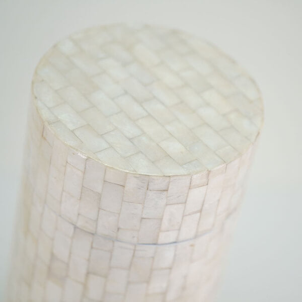 Close-up view of the top portion of a cylindrical scattering urn, showing a smooth, glossy surface made of small rectangular shell tiles arranged in a brick-like pattern.