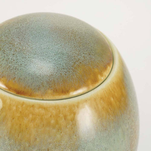 A close-up view of the Serene Reflections Ocean Blue Memorial Urn, available at Magnolia Cremations, highlighting its smooth, rounded lid and unique glaze pattern. The ceramic surface features a blend of ocean blue and warm brown hues, with a natural gradient effect that makes each urn one-of-a-kind.
