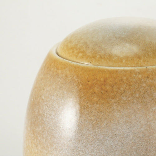 A close-up of the Serene Reflections Sandy White Memorial Urn, available at Magnolia Cremations, highlighting its smooth, rounded ceramic design with a unique beige and brown glaze. The subtle texture and organic color variations make each urn one-of-a-kind, offering a serene and elegant tribute.
