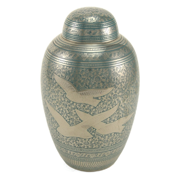 The Traditional Going Home Memorial Urn, available at Magnolia Cremations, is a full-size brass urn with a reflective nickel-plated finish and intricate hand-engraved detailing. The surface features an elegant silver and green floral pattern, with three gracefully soaring birds symbolizing peace and freedom. A domed lid with complementary engravings completes the classic, timeless design.