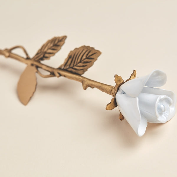 A close-up of the White Rose Keepsake from Magnolia Cremations, a finely crafted brass memorial piece with a smooth, white rose in full bloom. The golden-toned stem is adorned with textured leaves, adding to its lifelike appearance. This elegant keepsake is designed to discreetly hold a small portion of ashes, serving as a meaningful tribute to a loved one.