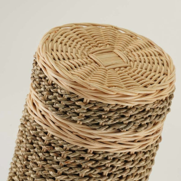 Close-up of the Woven Naturals Seagrass Memorial Urn, available at Magnolia Cremations. The image highlights the urn’s detailed craftsmanship, featuring a tightly woven seagrass body with a sturdy wicker lid. The lid showcases a symmetrical basketweave pattern in light beige, contrasting with the earthy brown seagrass below. A decorative wicker band encircles the top, reinforcing the structure while maintaining its organic aesthetic.