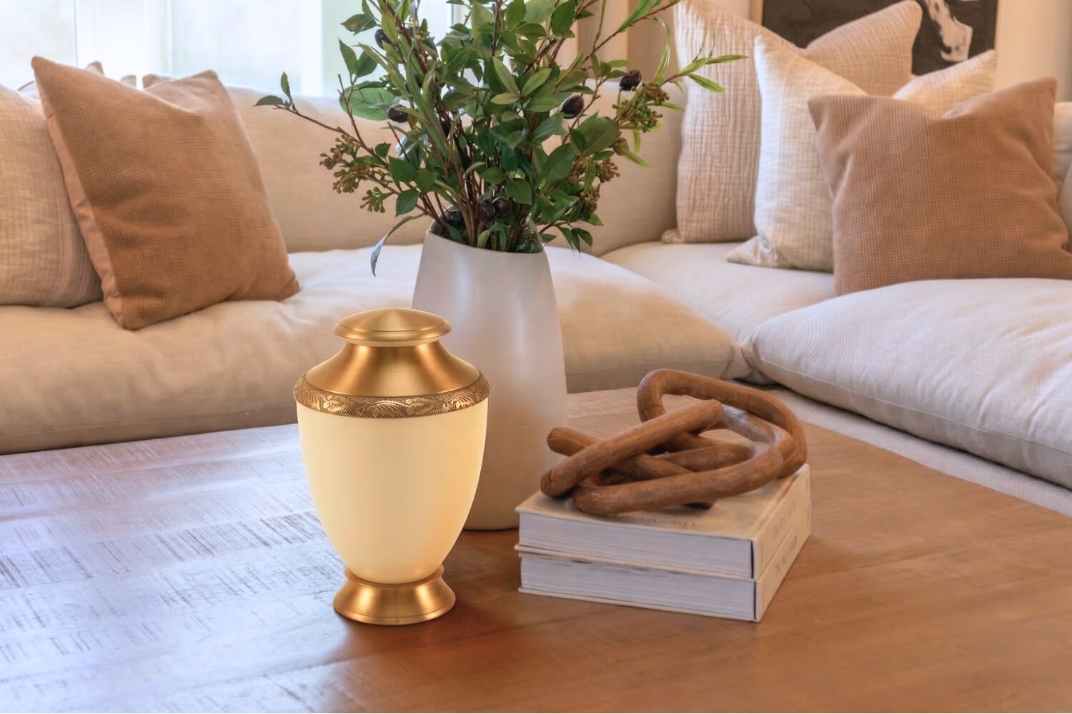 A cremation urn on a living room coffee table next to books and a vase with greenery