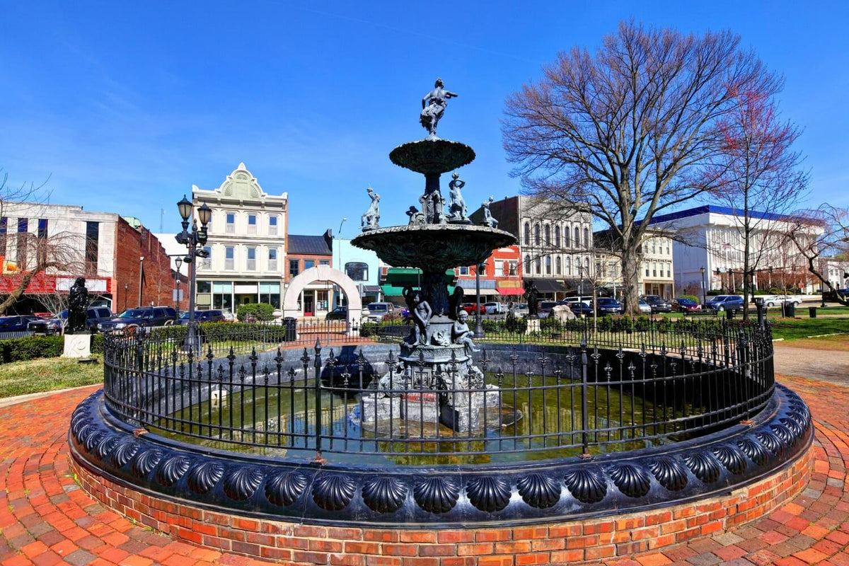 Fountain Square in downtown Bowling Green, KY, with historic buildings, parked cars, and leafless trees in the background under a clear blue sky.