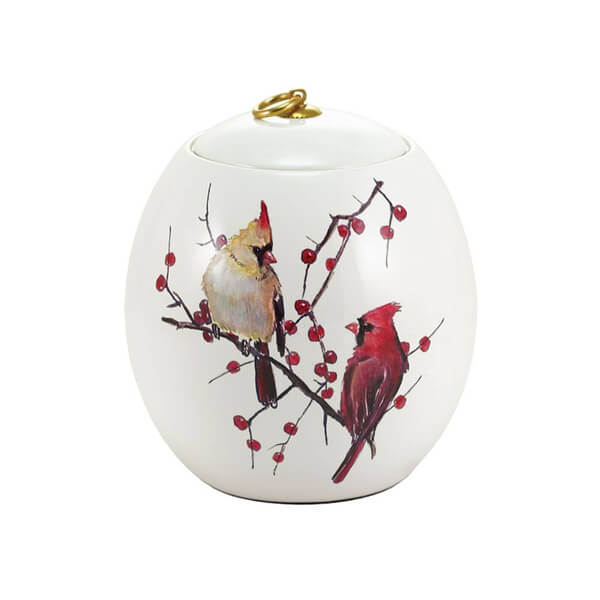 Decorative memorial cremation urn with cardinals and berries on a white background