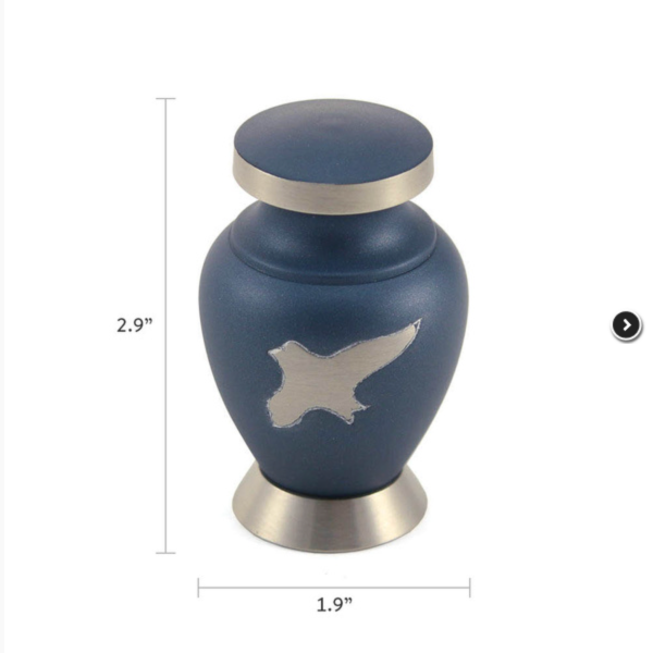 The Aria Ascending Keepsake Urn, available at Magnolia Cremations, is a small, navy blue urn with brushed silver accents. A silver inlaid bird in flight is featured on the front, symbolizing peace and freedom. The urn has a rounded shape with a slightly flared base and a matching silver-trimmed lid. Dimensions are shown, measuring approximately 2.9 inches in height and 1.9 inches in width, making it a compact and elegant option for holding a small portion of ashes.