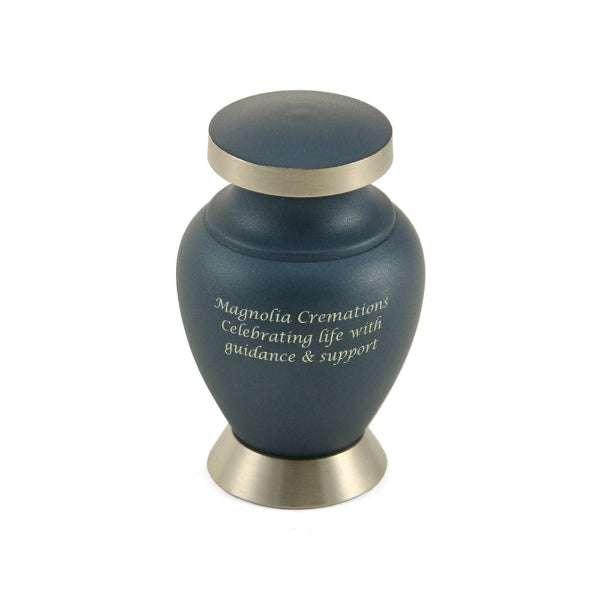 The Aria Ascending Keepsake Urn, available at Magnolia Cremations, is a small, classic urn with a matte navy blue finish. It features a brushed silver-tone base, lid, and trim, giving it a sophisticated contrast. The urn is shown with engraved text, indicating that personalization is available. Designed to hold a small portion of ashes, this keepsake urn offers a meaningful way to share a loved one’s memory among family and friends.