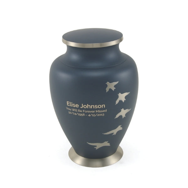 The Aria Ascending Memorial Urn from Magnolia Cremations, is a full-size cremation urn with a matte navy blue finish, accented by a brushed silver-tone base and lid. A series of silver birds in flight are etched along the side, symbolizing peace and transition. A personalized engraving is featured on the front, making this urn a meaningful and elegant tribute to a loved one.