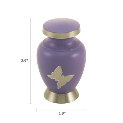 The Aria Butterfly Keepsake Urn from Magnolia Cremations is a petite memorial urn designed to hold a small portion of ashes, allowing multiple family members to keep a tangible remembrance of their loved one. The urn features a soft lavender matte finish, a brushed silver butterfly emblem, and silver trim on the base and lid. Dimensions are shown, indicating a height of 2.9 inches and a width of 1.9 inches.