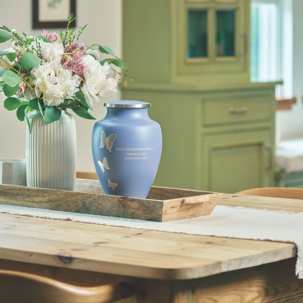 Lavender Aria cremation urn displayed on a wooden table with floral arrangement in the background.