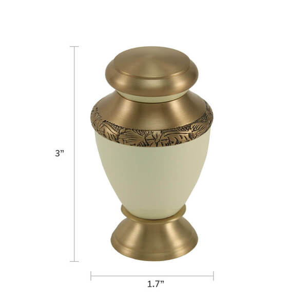 The Artisan Pearl Keepsake Urn, available at Magnolia Cremations, is a small yet elegant memorial piece featuring a soft pearl-white body with gold-tone accents. A delicately engraved floral band encircles the upper portion, complementing the urn’s timeless design. Its rounded shape, flared base, and domed lid add to its refined appearance. Measurement lines indicate its compact dimensions of approximately 3 inches tall and 1.7 inches wide, making it ideal for holding a small portion of a loved one’s ashes 