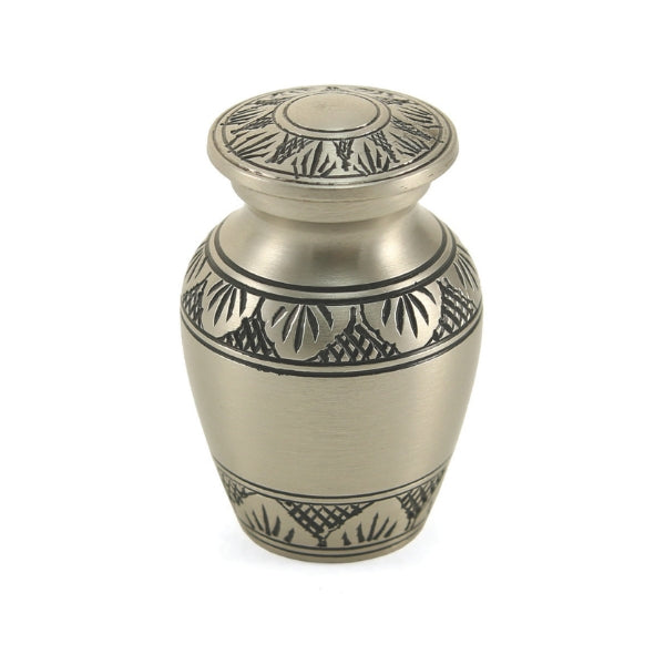 The Athena Pewter Keepsake Urn, available from Magnolia Cremations, is a small memorial urn with a classic silver-tone finish and intricate black leaf engravings. Part of the Classic Athena Collection, this keepsake allows families to share a portion of their loved one’s ashes, keeping their memory close in a refined and timeless design.