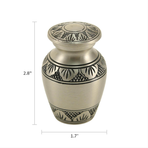 The Athena Pewter Keepsake Urn, available from Magnolia Cremations, is a small memorial urn with a brushed silver finish and intricate black leaf engravings. The image includes dimensions, showing the urn is 2.8 inches tall and 1.7 inches wide. Designed to hold a small portion of ashes, this keepsake allows family members to share a meaningful remembrance of their loved one.