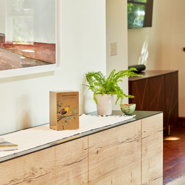 Memorial urn with personalized engraving displayed on a modern wooden cabinet, surrounded by home decor