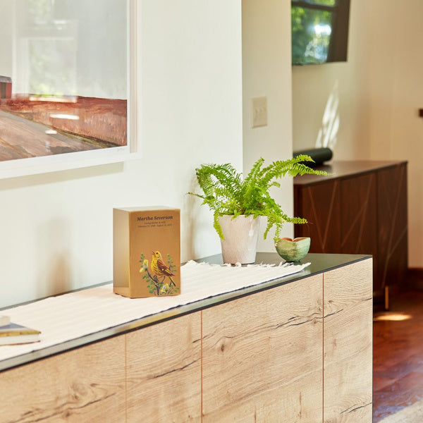 The companion urn displayed on a modern wooden sideboard, surrounded by natural decor, creating a warm and serene memorial setting.