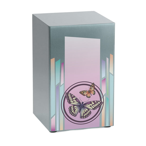 Life Canvas Butterflies Pewter Full-Size Cremation Urn. A rectangular stainless-steel urn with a brushed silver finish, featuring a soft pink and lavender gradient panel adorned with two detailed butterflies enclosed in a circular accent. Vertical pastel geometric patterns add an elegant touch. Designed for home display and can be personalized with engraving. 200 cubic inch capacity.