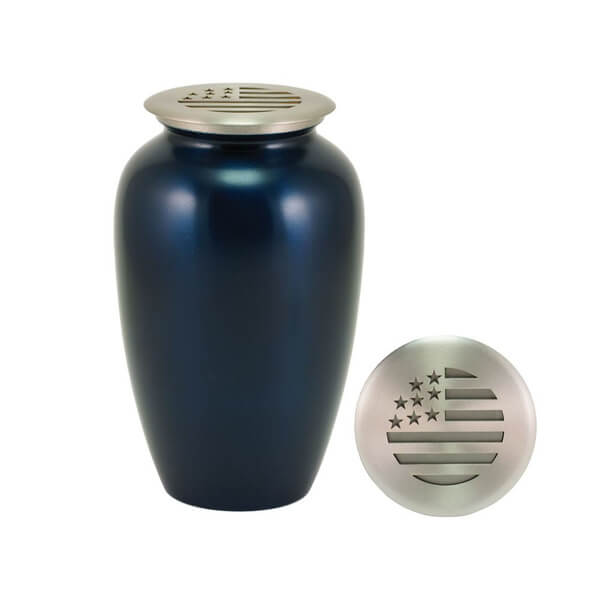 A dark blue scattering urn with a silver-toned lid. The lid features a cutout design resembling the American flag, with stars and stripes. An additional view of the lid is shown beside the urn to highlight the flag design.