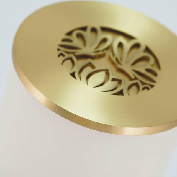 Close-up view of a metallic gold lid with an intricate cut-out design featuring two symmetrical butterflies facing each other. The lid is attached to a cream-colored cylindrical container.