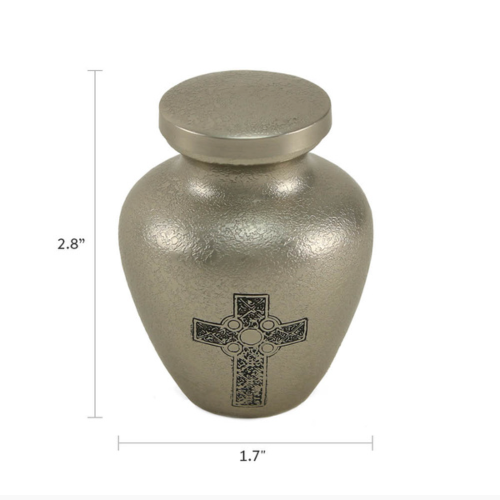 The Celtic Cross Keepsake Urn, offered by Magnolia Cremations, is a small, textured silver urn featuring a detailed black Celtic Cross engraving on the front. Measuring 2.8 inches in height and 1.7 inches in width, this brass keepsake is designed to hold a small portion of ashes, allowing families to keep a cherished remembrance of their loved one.