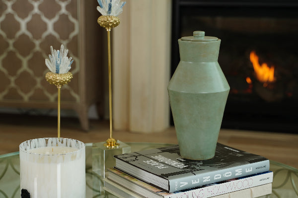 Deco Pure Forest Full-Size Cremation Urn by Stoneware & Co. displayed on a glass coffee table in an elegant living room. This handcrafted ceramic urn in deep forest green features an Art Deco-inspired design with clean lines and a natural finish. A warm fireplace and decorative accents create a serene setting. Suitable for individuals weighing up to 210 lbs.