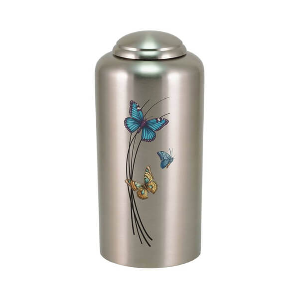 Silver-colored cremation urn with a domed lid, featuring a design of three colorful butterflies—blue, teal, and orange—flying around curved black lines resembling tall grass.