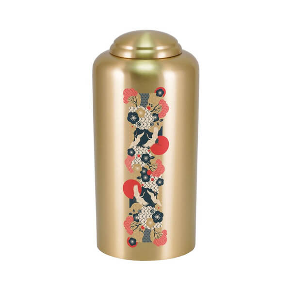 Gold-colored cremation urn with a domed lid, featuring a vertical decorative panel on the front. The panel displays an intricate crane design with red, black, and white accents, surrounded by floral and fan motifs in a traditional Japanese-inspired style.