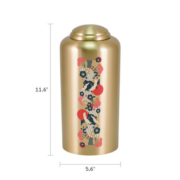 Gold-colored cremation urn with a domed lid, measuring 11.6 inches tall and 5.6 inches wide. The front features a vertical Japanese-inspired design with black and white cranes, red suns, and various floral and fan motifs in red, black, and gold tones.