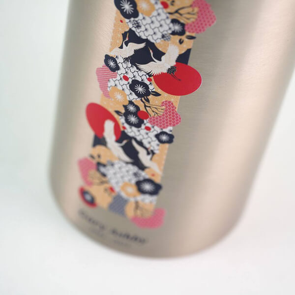 Close-up view of a silver cremation urn showing a detailed vertical decorative panel. The design features white cranes in flight, red sun motifs, and a mix of floral and wave patterns in red, navy blue, white, and gold, inspired by traditional Japanese art.