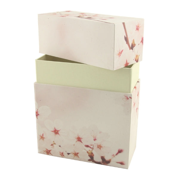 An eco-friendly memorial urn with a cherry blossom design, shown with its lid removed to reveal a light-colored interior. The rectangular urn is designed for scattering or burial, featuring a two-piece construction. Engraving is not available.
