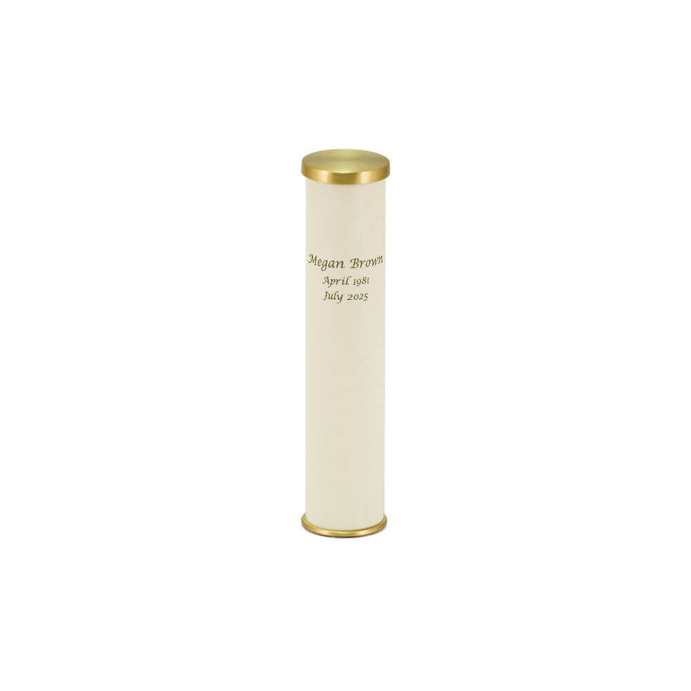 A cylindrical scattering keepsake urn with a cream-colored body and gold-colored top and bottom caps. The urn is engraved with the name "Megan Brown" and the dates "April 1981 – July 2025."