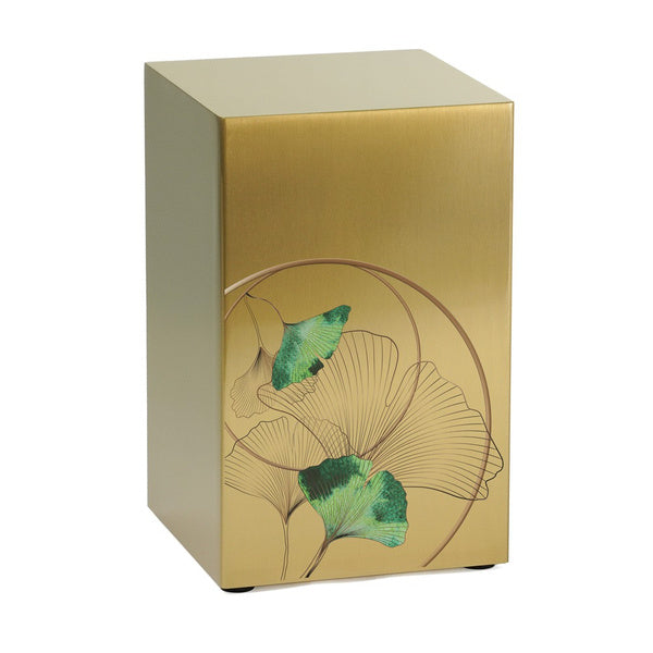 A contemporary memorial urn with a brushed gold finish, featuring an artistic ginkgo leaf design with intricate linework and vibrant green accents. The rectangular stainless steel urn is part of the Life Canvas Series and can be displayed alone or as part of a companion set.