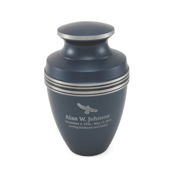 A matte blue urn with silver accent bands and a matching lid. The urn has engraved text and an emblem on the front, with engraving available for personalization. It has a classic shape with a slightly tapered base and a rounded top.