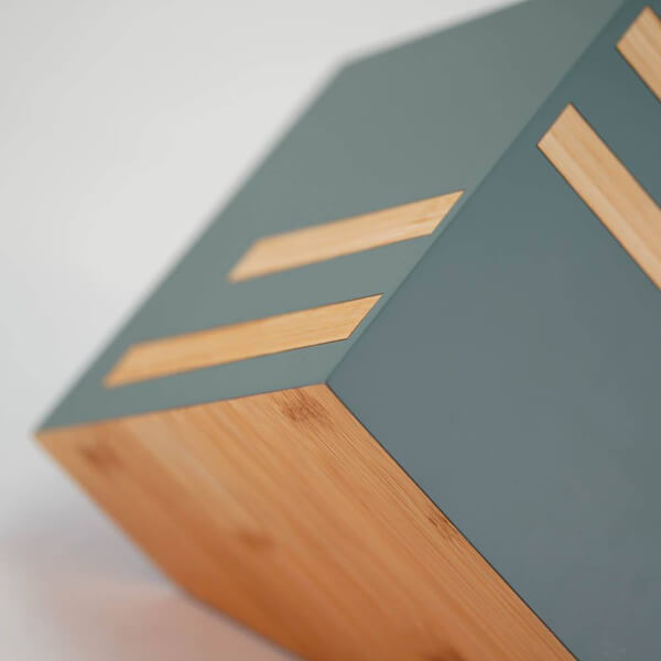 Close-up view of a modern cremation urn with sage green sides and natural bamboo accents. The design features clean lines, with horizontal bamboo inlays and a bamboo base, emphasizing a minimalist, geometric aesthetic.