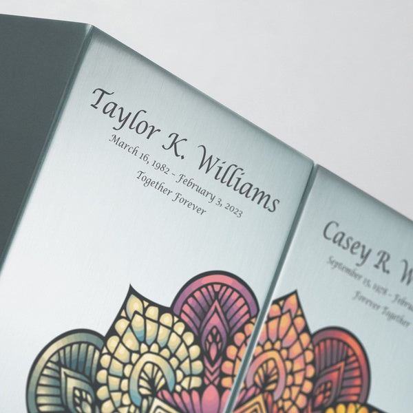 Close-up of the Mandala in Pewter Companion Urns from Magnolia Cremations, showcasing personalized engraving on a sleek brushed pewter surface. The intricate mandala design in warm, vibrant hues adds a meaningful and artistic touch, symbolizing unity and remembrance. This contemporary cremation urn set is a perfect tribute for loved ones wishing to be memorialized together, offering both elegance and personalization in a timeless design.