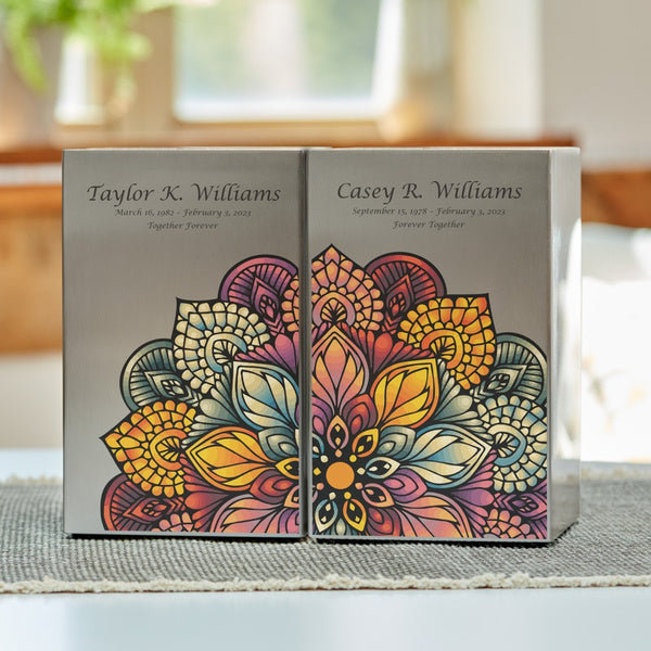 Mandala in Pewter Companion Urn Set by Magnolia Cremations, displayed side by side on a neutral woven mat. These matching cremation urns feature a brushed pewter finish with an intricate and colorful mandala design, symbolizing unity and remembrance. Each urn is engraved for personalization, creating a heartfelt tribute for loved ones. Designed for companion memorials, this set offers a contemporary and meaningful way to honor a shared legacy.